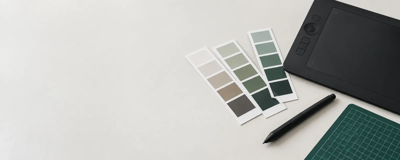 Colour swatch strips fanned across a pale desk beside a graphics tablet, stylus and green cutting mat