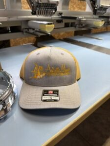 Tan and white cap with an embroidered chest logo on a workbench